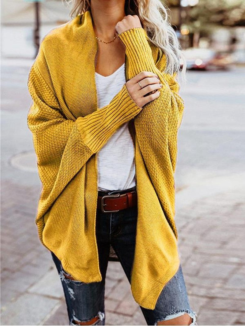 Woman wearing a mustard yellow chunky knit cardigan over a white top and ripped jeans with a brown belt