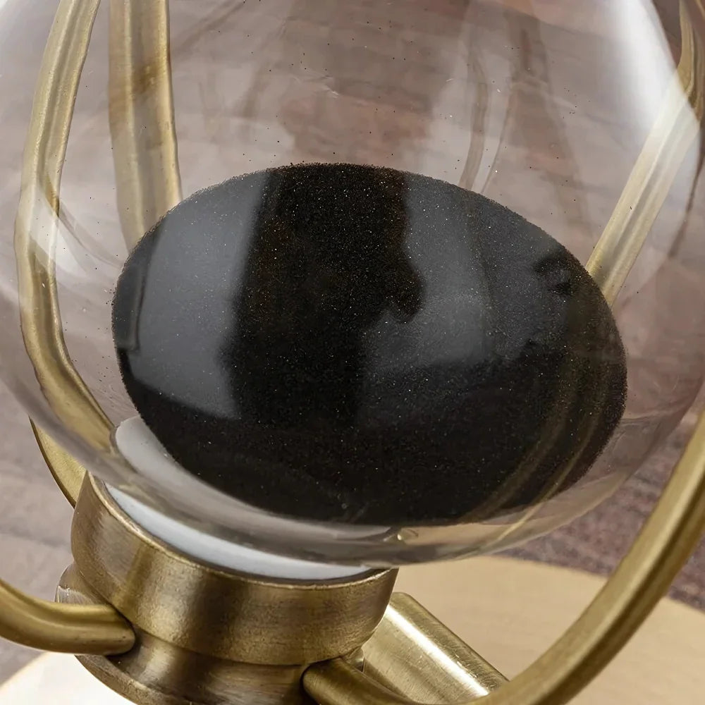 Close-up of black sand in a golden metal hourglass on a wooden surface