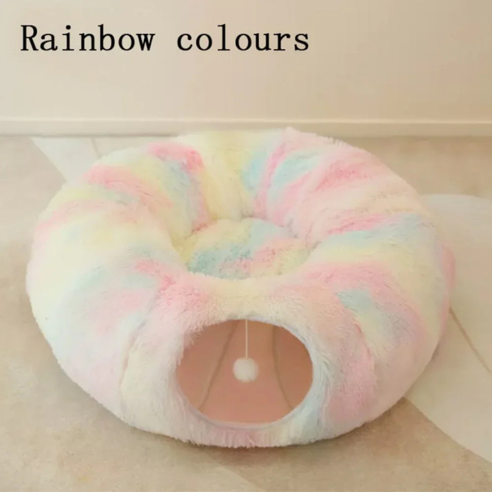 Rainbow-colored plush circular pet bed with a small tunnel and hanging pom pom toy