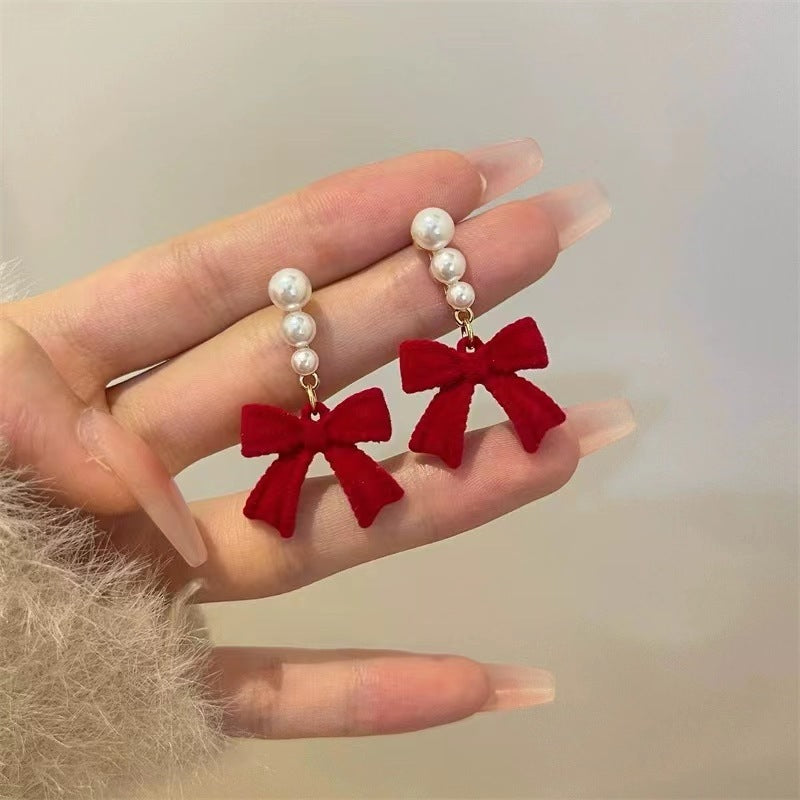 Red bow earrings with pearl details held in a hand against a neutral background