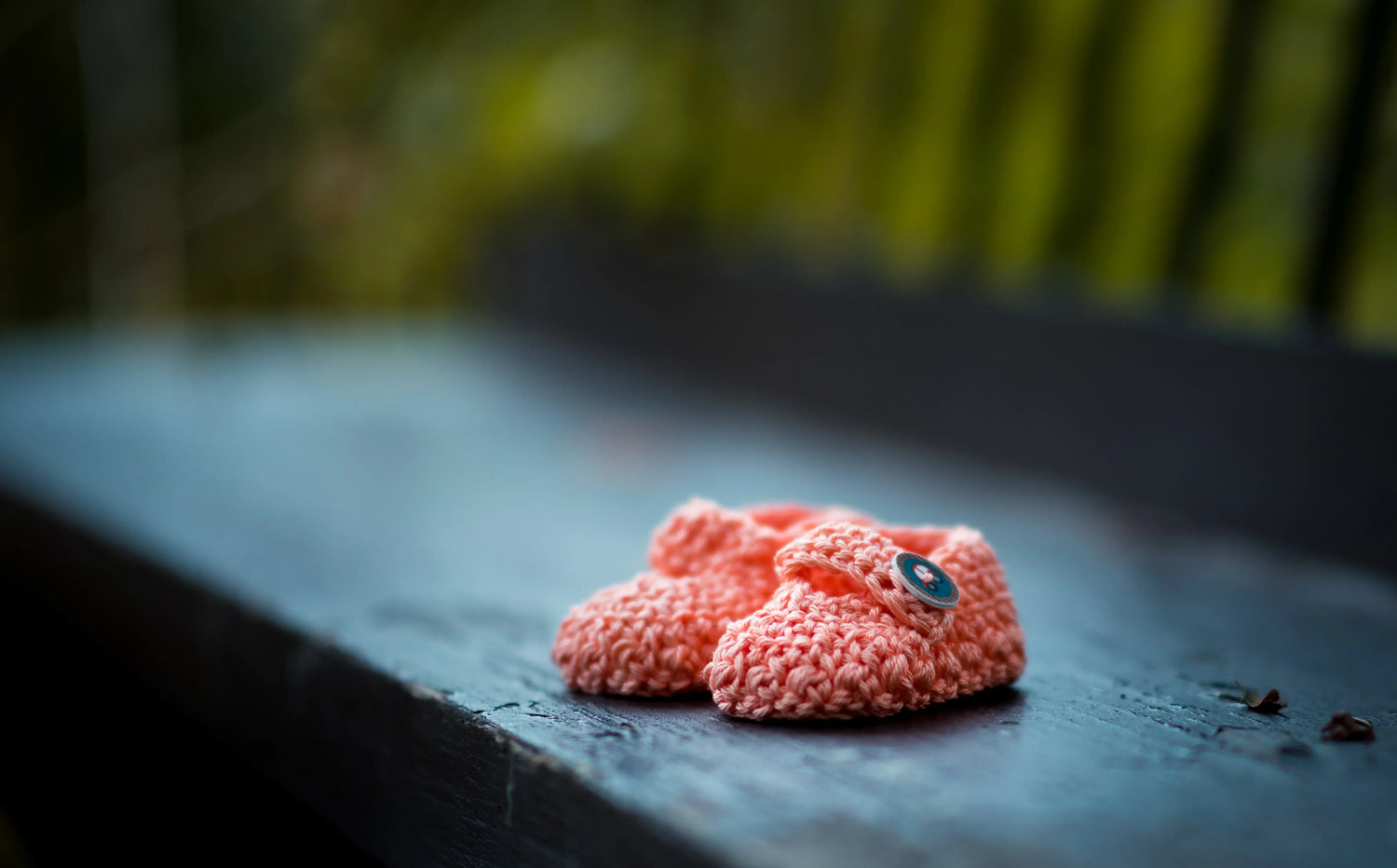 Pair of handmade pink crocheted baby booties with buttons on a dark wooden surface