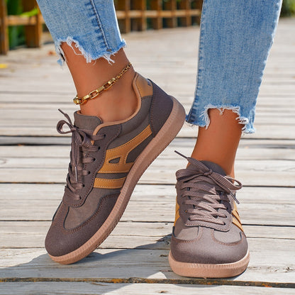 Close-up of brown and beige sneakers worn with ripped light blue jeans and a gold ankle bracelet on wooden deck