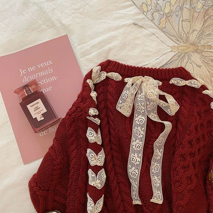 Red sweater with lace details on a white surface next to a pink book with a perfume bottle illustration.
