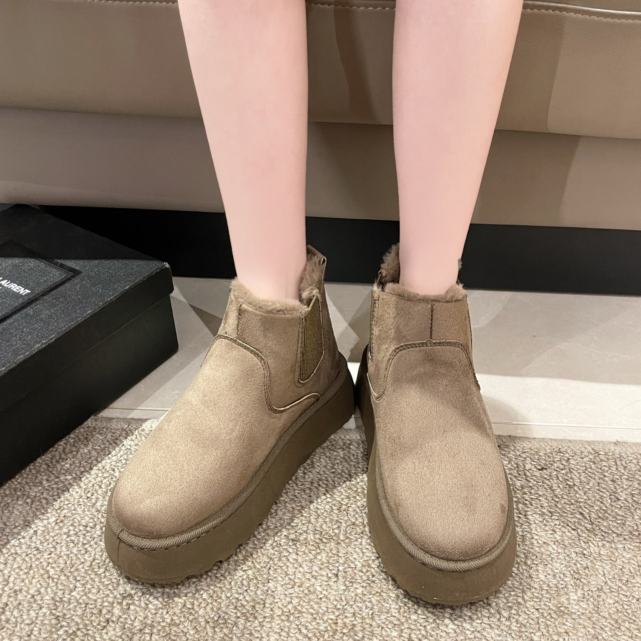 Pair of tan suede winter boots with fur lining worn indoors on carpeted floor