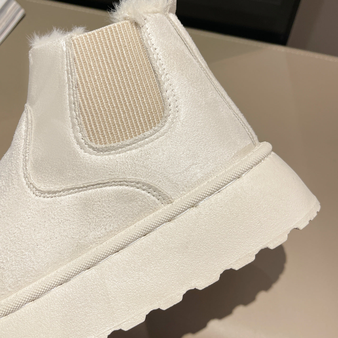 Close-up of a beige suede ankle boot with elastic side panel and textured rubber sole