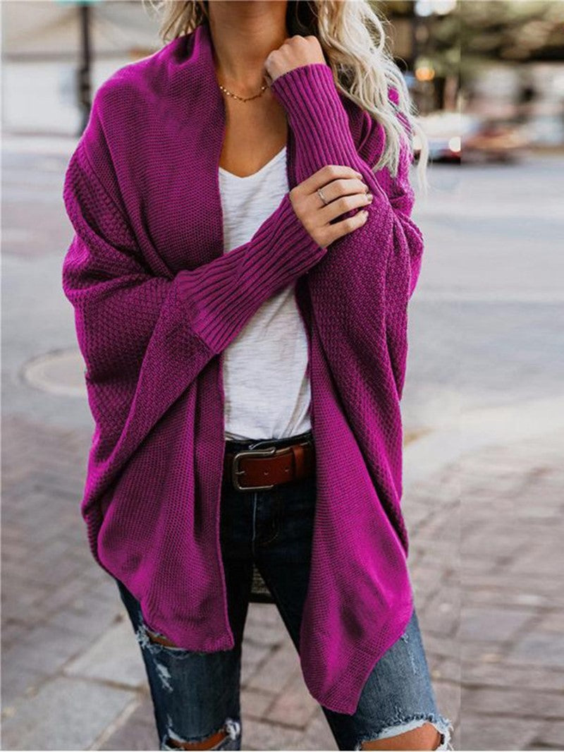 Woman wearing a magenta knitted cardigan over white t-shirt and ripped jeans on city street