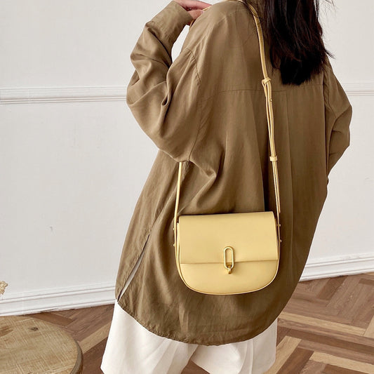 Woman wearing a loose brown shirt and white skirt with a beige leather crossbody bag indoors