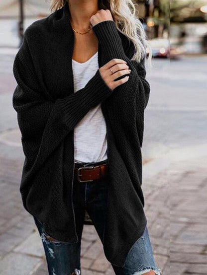 Woman wearing black oversized knit cardigan, white t-shirt, distressed jeans, and brown belt on urban sidewalk