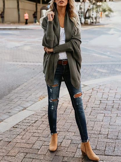 Woman wearing an oversized olive cardigan, white top, ripped skinny jeans, and tan ankle boots on city street