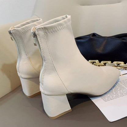 Pair of white leather ankle boots with block heels and back zippers on a beige surface