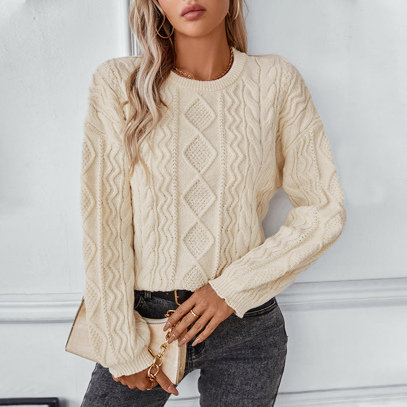 Woman wearing a cream cable knit sweater with diamond patterns, paired with dark jeans and gold accessories