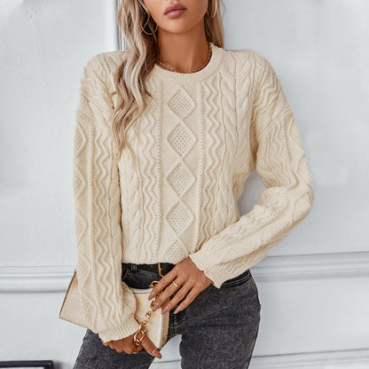 Woman wearing a cream cable knit sweater with diamond patterns, paired with dark jeans and gold accessories