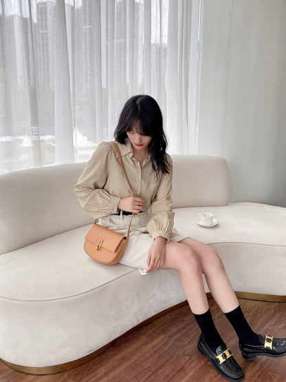 Woman in beige blouse and skirt with tan purse sitting on white curved sofa by sheer curtains