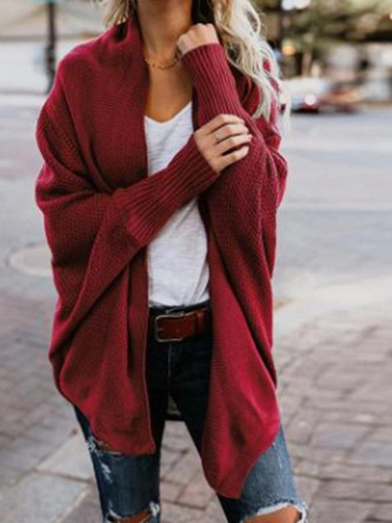 Woman wearing oversized red knit cardigan over white t-shirt and ripped jeans on city street