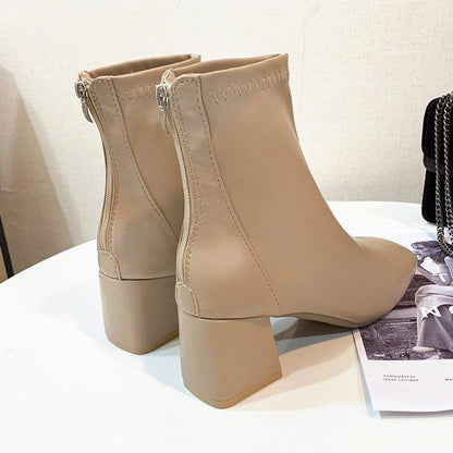 Beige leather ankle boots with block heels and back zipper, displayed on white table