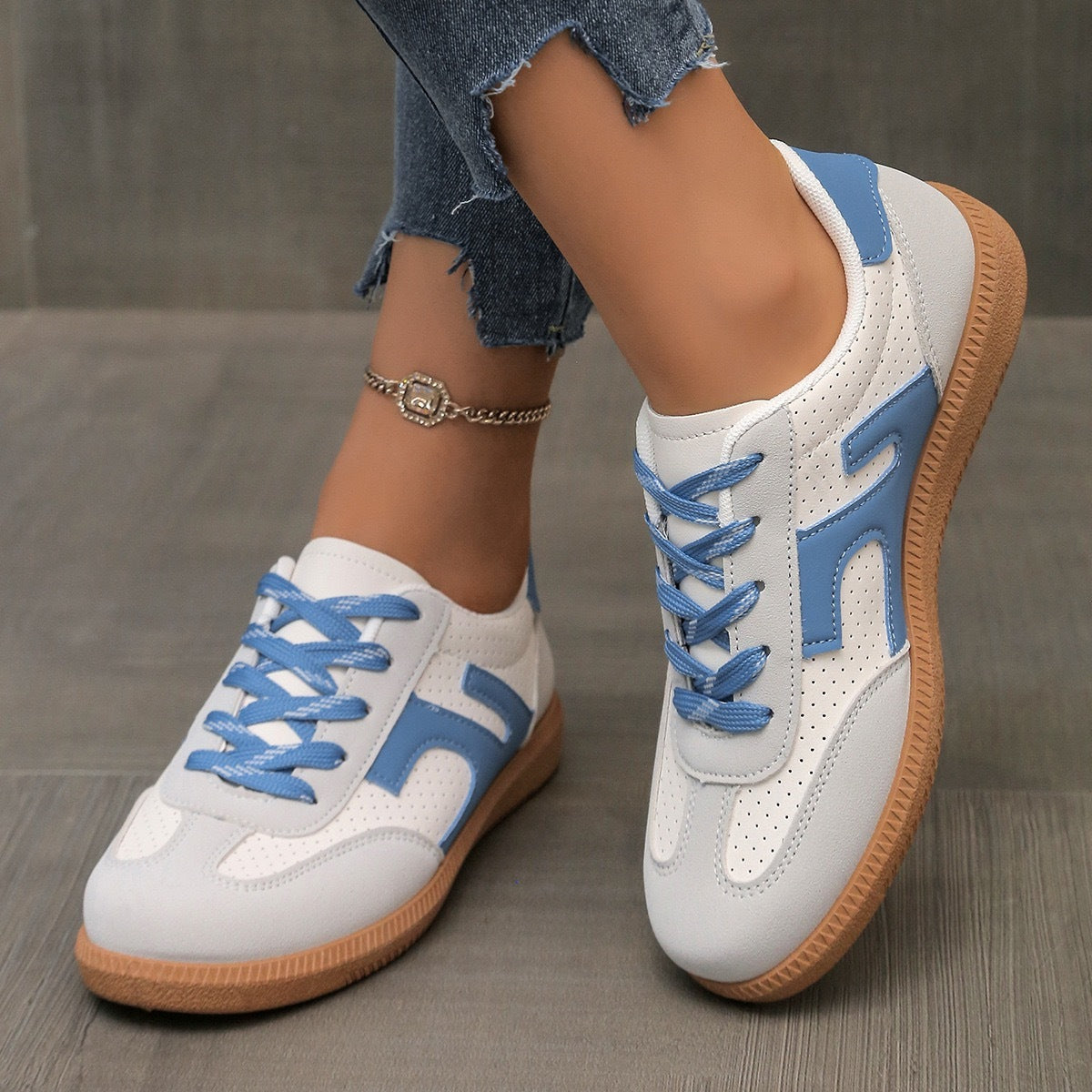 White and blue casual sneakers with gum soles worn with ripped denim jeans and a gold anklet