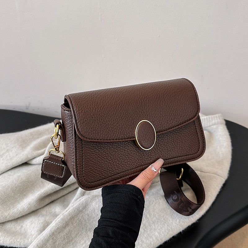 Dark brown textured leather crossbody bag with gold oval clasp and adjustable strap