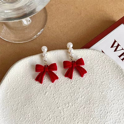 Red bow earrings with pearl accents on a textured surface