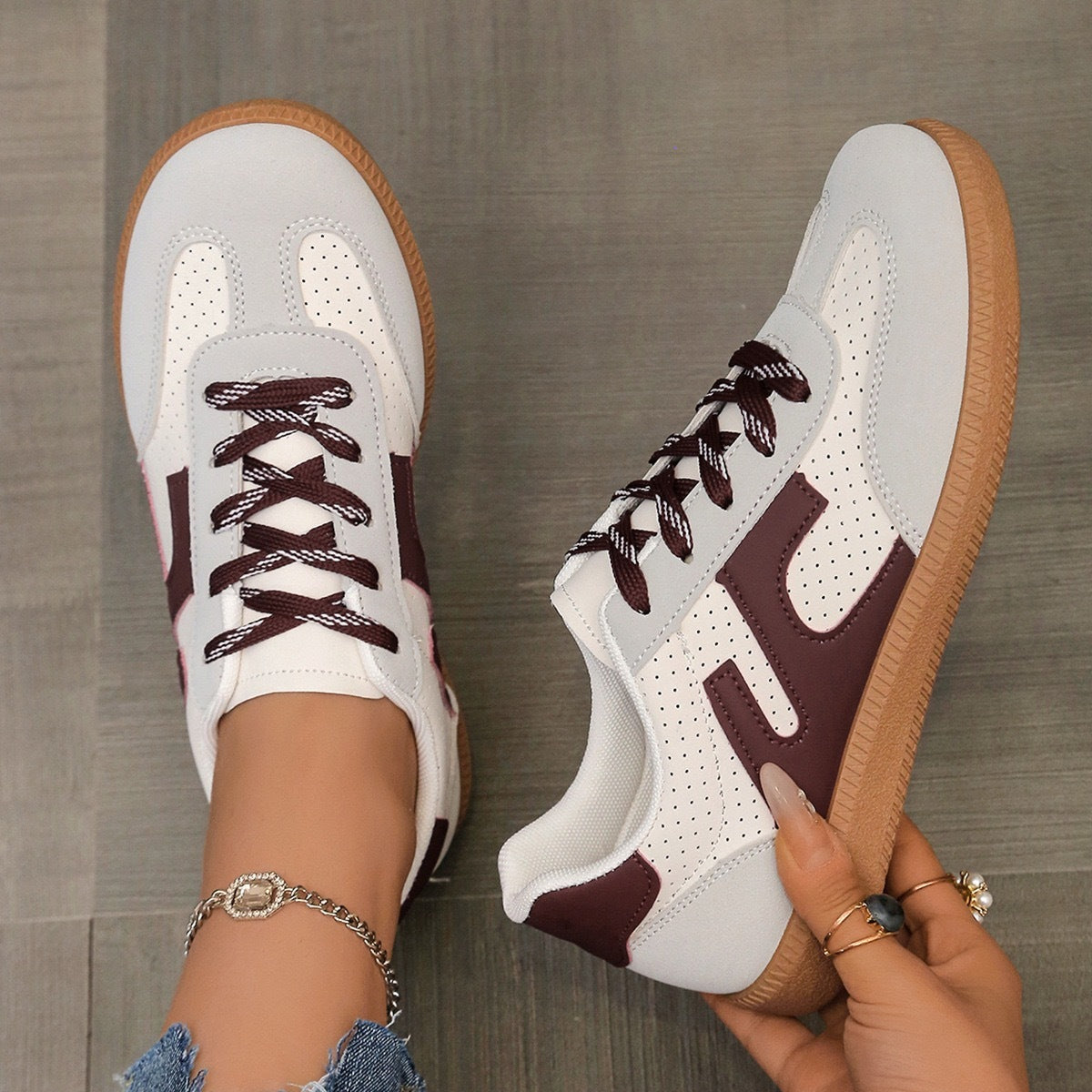 White and burgundy casual sneakers with perforated details and gum soles on wooden floor