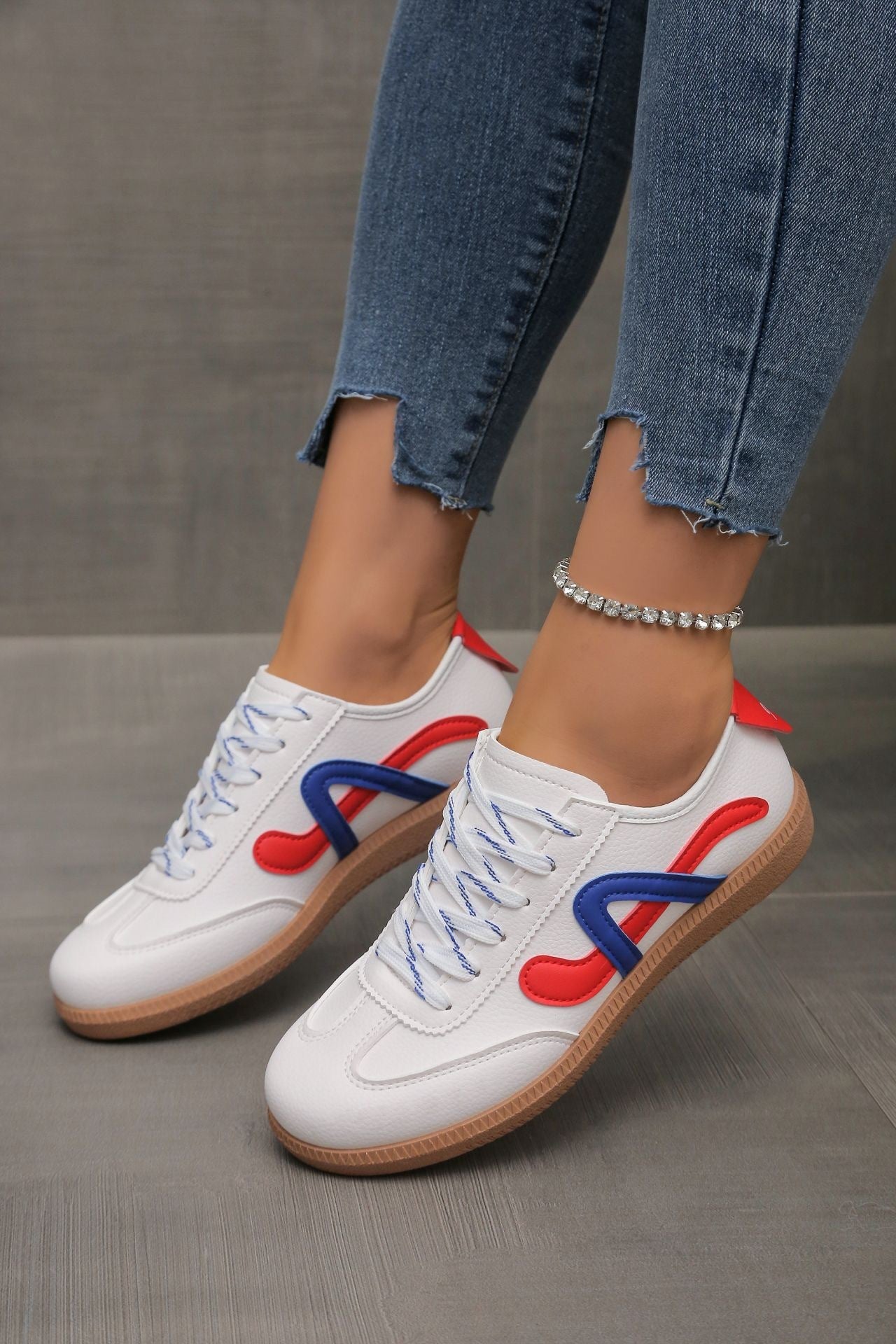White casual sneakers with blue and red accents on feet wearing frayed hem jeans and a rhinestone anklet