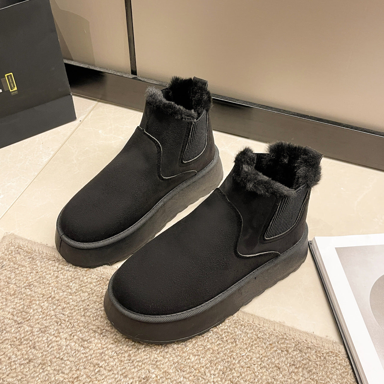 Pair of black suede winter boots with fur lining and thick sole placed on beige tile floor near carpet