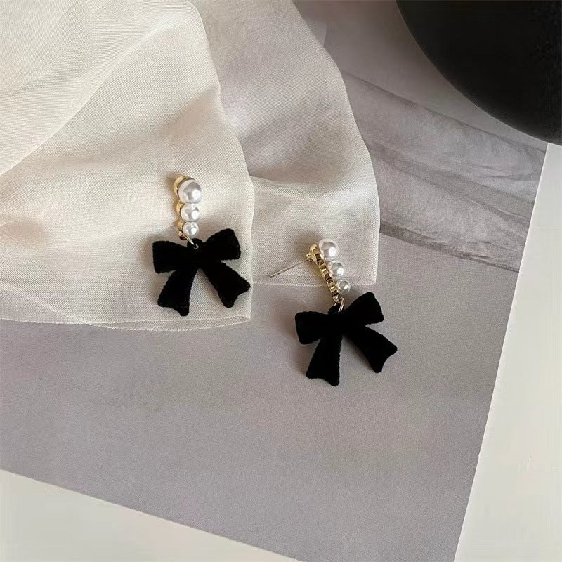 Black bow earrings with pearl details on a light fabric background