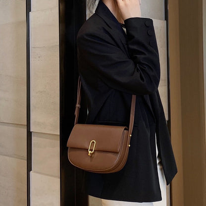 Woman in black blazer carrying brown leather shoulder bag with gold clasp indoors