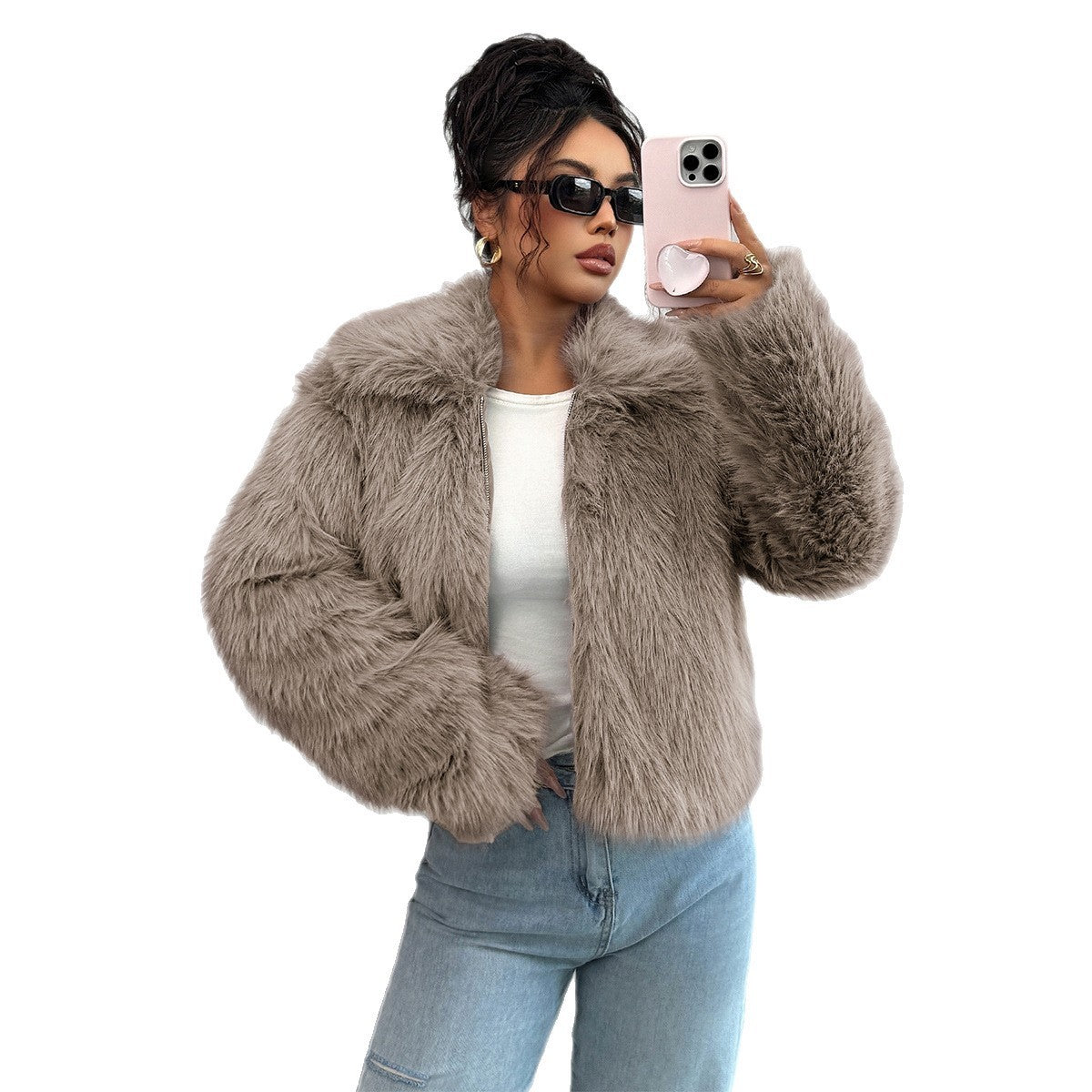 Woman in oversized taupe faux fur jacket, white top, blue jeans, sunglasses taking selfie with pink phone