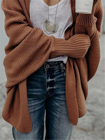 Woman wearing rust brown chunky knit cardigan, white t-shirt, high-waisted blue jeans, and silver pendant necklace