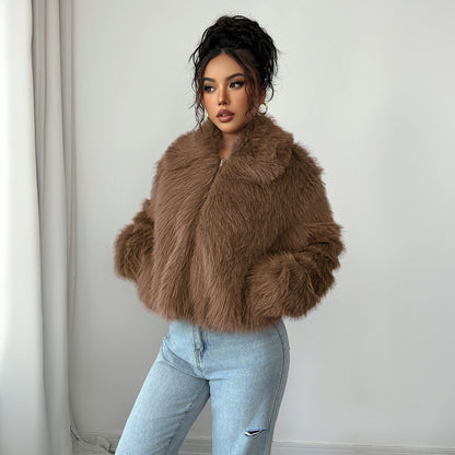 Woman wearing brown faux fur jacket and light blue ripped jeans standing against white wall