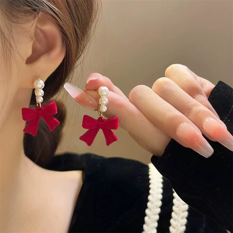 Close-up of a person wearing red bow earrings with pearl accents.