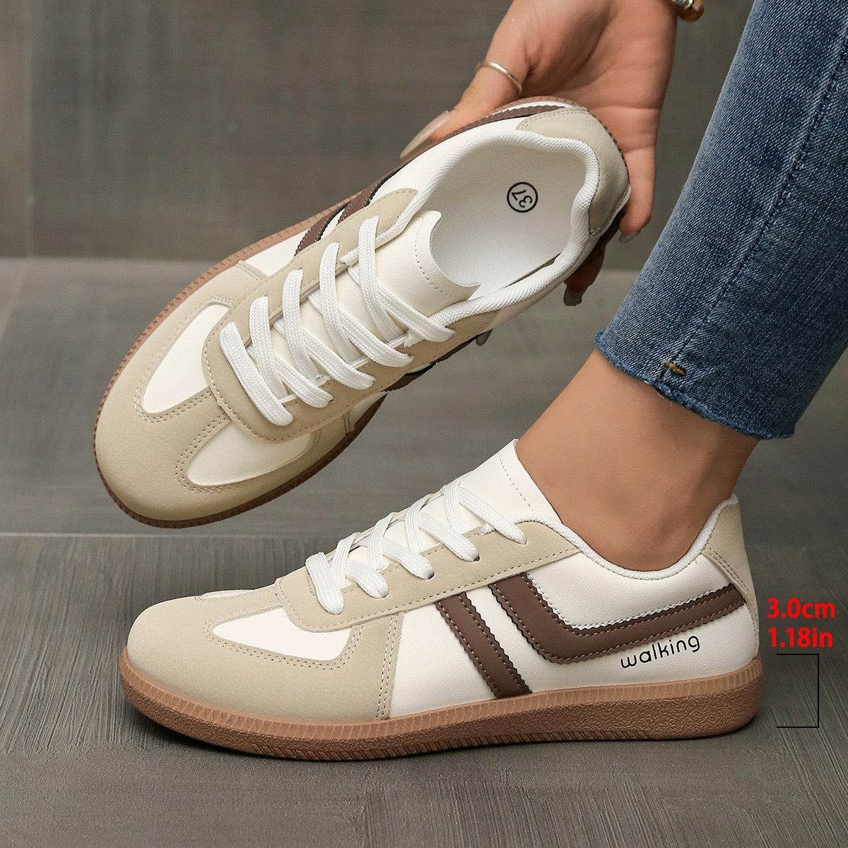 Casual beige and white walking sneakers with brown accents, worn with jeans on wooden floor