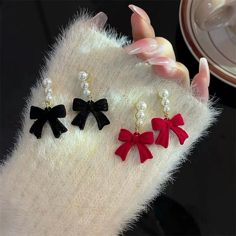 Pair of earrings with black and red bows held over a fluffy white surface.