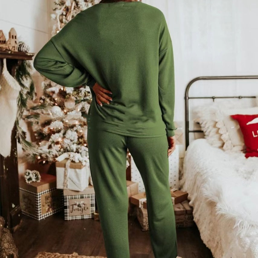 Person wearing a green outfit standing in a bedroom with a bed and decorative items.