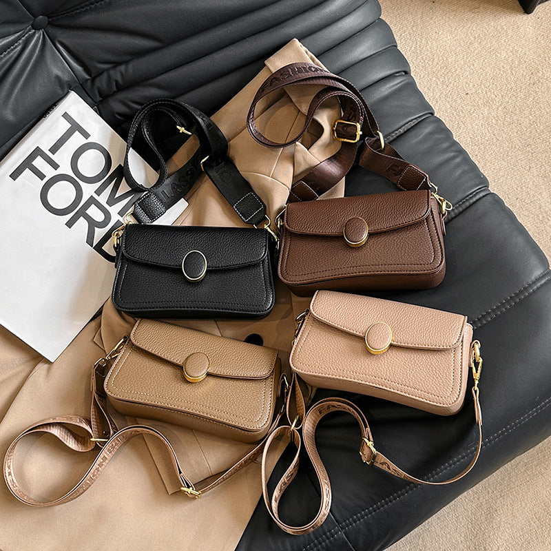 Four small leather crossbody bags in black, brown, beige, and cream on a black leather couch with a beige coat and Tom Ford packaging