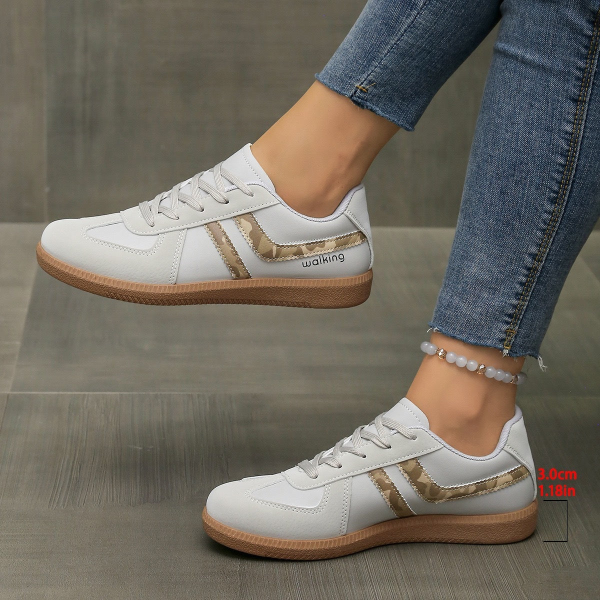 White casual sneakers with beige camouflage stripe and brown sole worn with blue jeans
