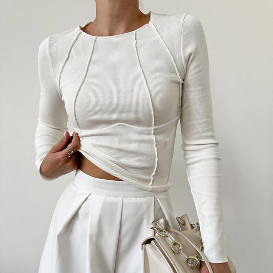Person wearing a white long-sleeve top and white pants, holding a beige handbag against a plain background.