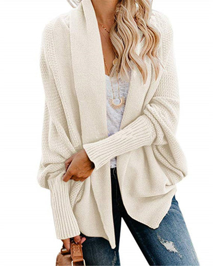 Woman wearing cream knit cardigan with ribbed sleeves, white top, ripped jeans, holding brown handbag