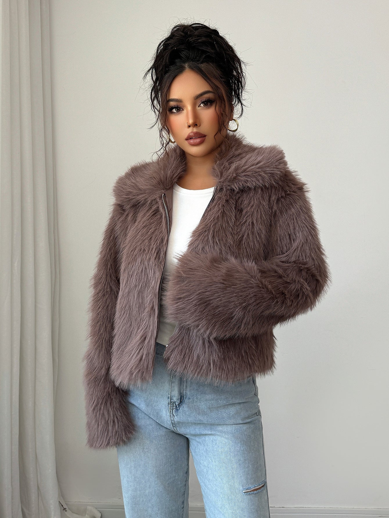 Woman in mauve faux fur jacket, white top, and light blue jeans against plain white background