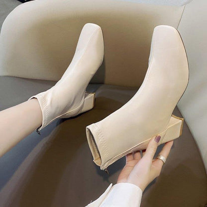 Beige high-heeled ankle boots with square heels worn on a sofa, stylish women's fashion footwear