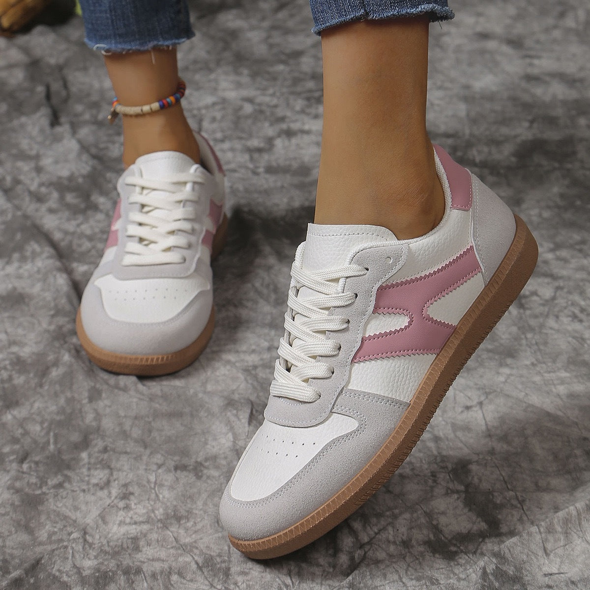 White and pink leather sneakers with beige suede and gum sole worn with cropped jeans on gray textured floor