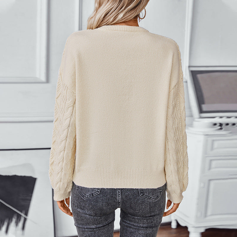 Woman wearing cream knit sweater with textured cable sleeves and gray jeans, back view