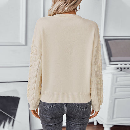 Woman wearing cream knit sweater with textured cable sleeves and gray jeans, back view