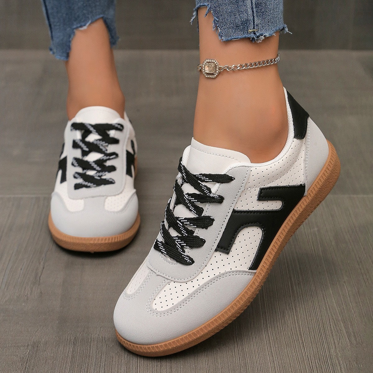 White and black casual sneakers with gum soles worn with frayed denim jeans and a gold anklet