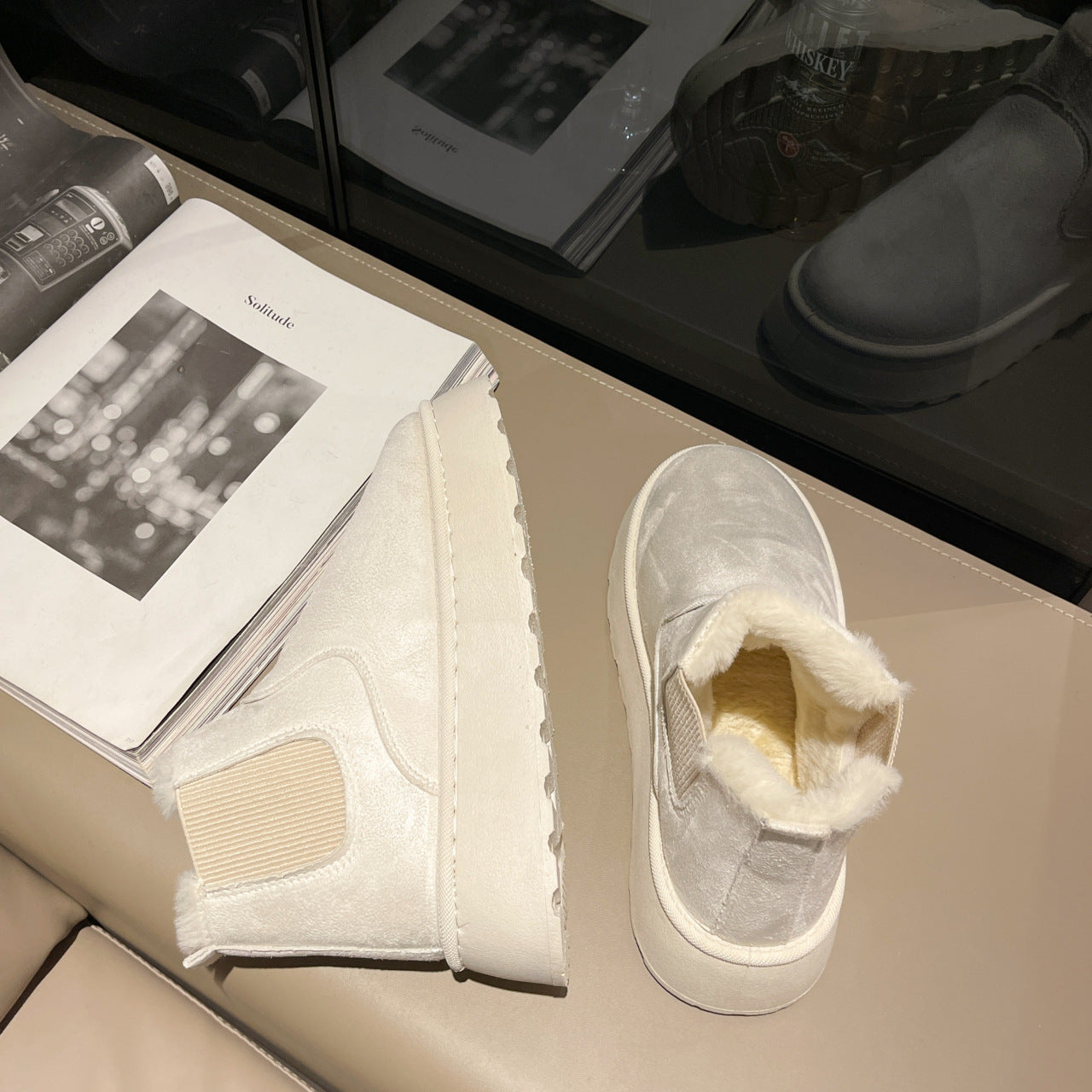 Cream-colored suede winter boots with plush fur lining on beige surface next to open magazine