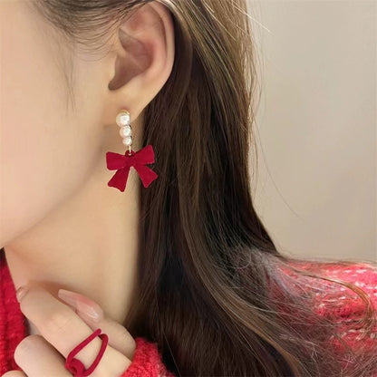 Red bow earrings worn by a person with a neutral background