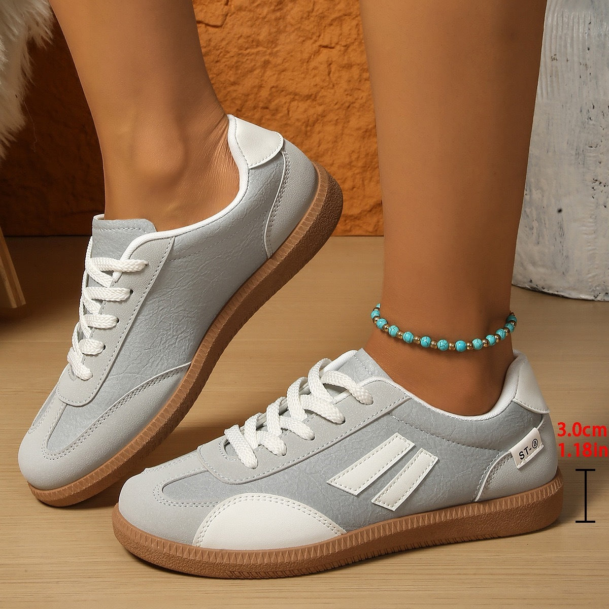 Light gray casual sneakers with white accents and gum soles worn with turquoise bead anklet