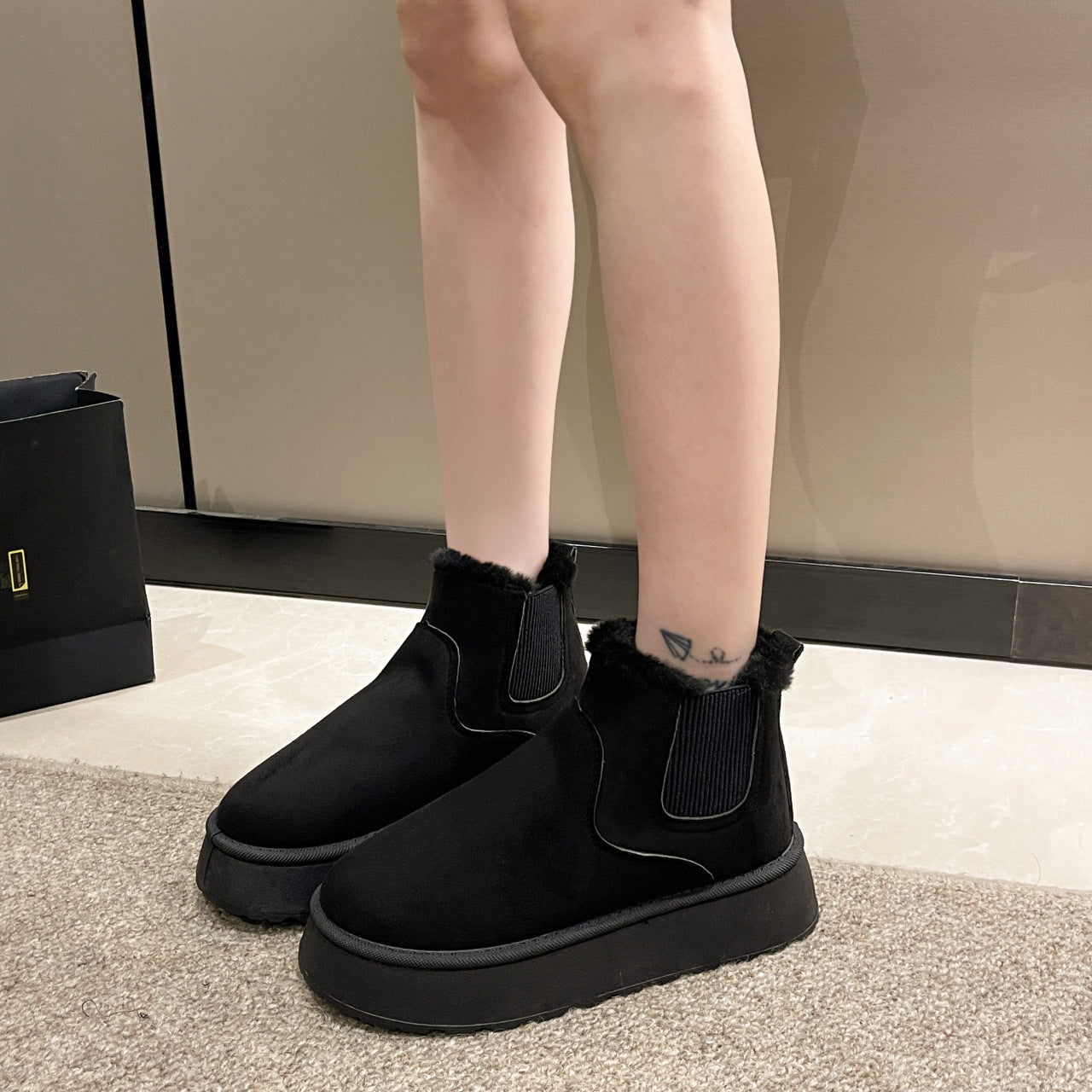 Person wearing black platform ankle boots with fur lining and elastic sides indoors on carpet