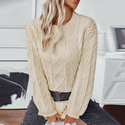 Woman wearing cream cable knit sweater and dark jeans holding beige clutch indoors