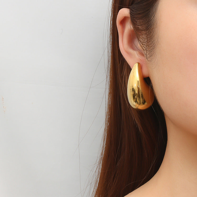 Close-up of a woman's ear wearing a large shiny gold teardrop hoop earring with long brown hair